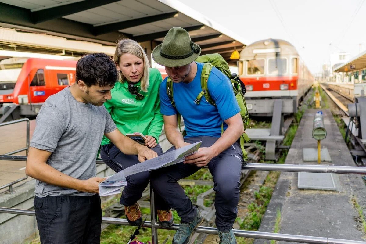 Viele Bergziele sind gut mit Bus und Bahn zu erreichen. | © DAV / Hans Herbig 3 Wandernde, die an einem Bahnhof sitzen und in eine Wanderkarte schauen. | © DAV / Hans Herbig