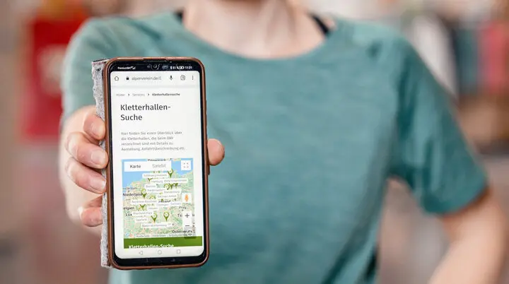 Eine Frau hält ihr Smartphone in die Kamera - auf dem Display sieht man die Kletterhallensuche | © DAV/Marisa Koch